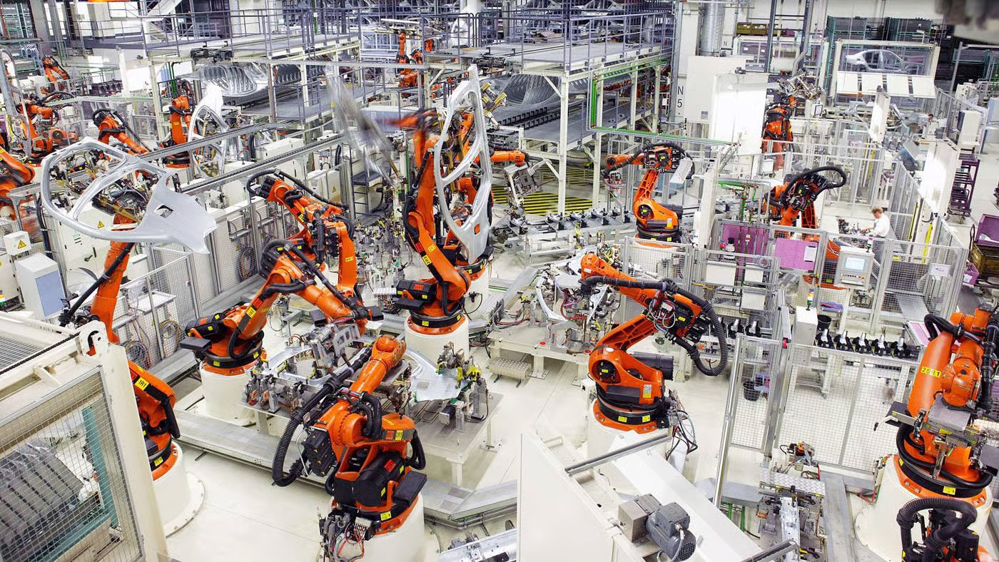 Row of orange KUKA robot arms working on an automated factory floor